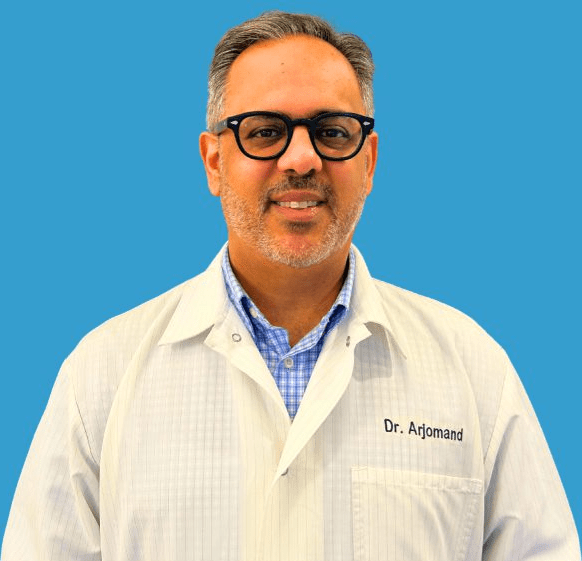 A smiling man, Dr. Arjomand, in a lab coat and glasses, against a blue background